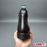 Hand holding the back of a black Chelsea boot, highlighting the heel tab and practical inner zipper for easy wear.