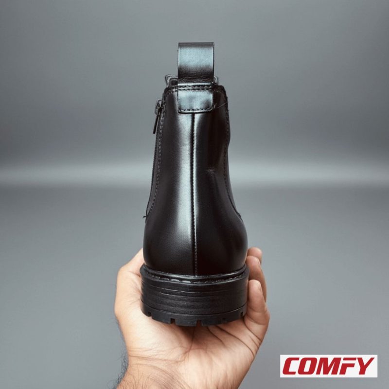 Hand holding the back of a black Chelsea boot, highlighting the heel tab and practical inner zipper for easy wear.