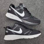 A pair of Shadow Zoom black running shoes with white swooshes and soles, laid out side-by-side on a textured gray fabric.