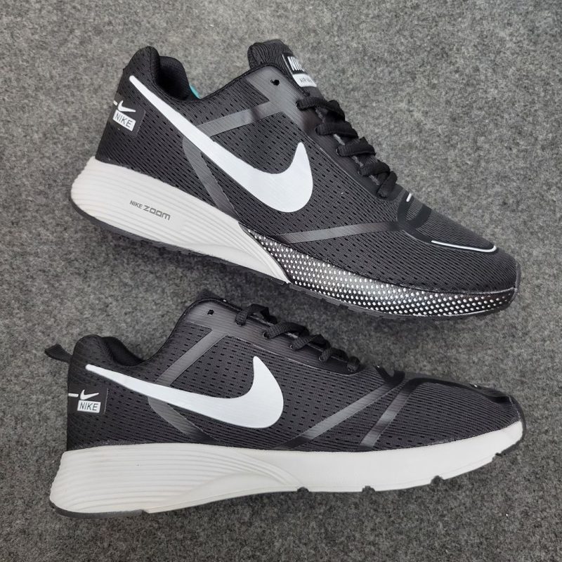 A pair of Shadow Zoom black running shoes with white swooshes and soles, laid out side-by-side on a textured gray fabric.