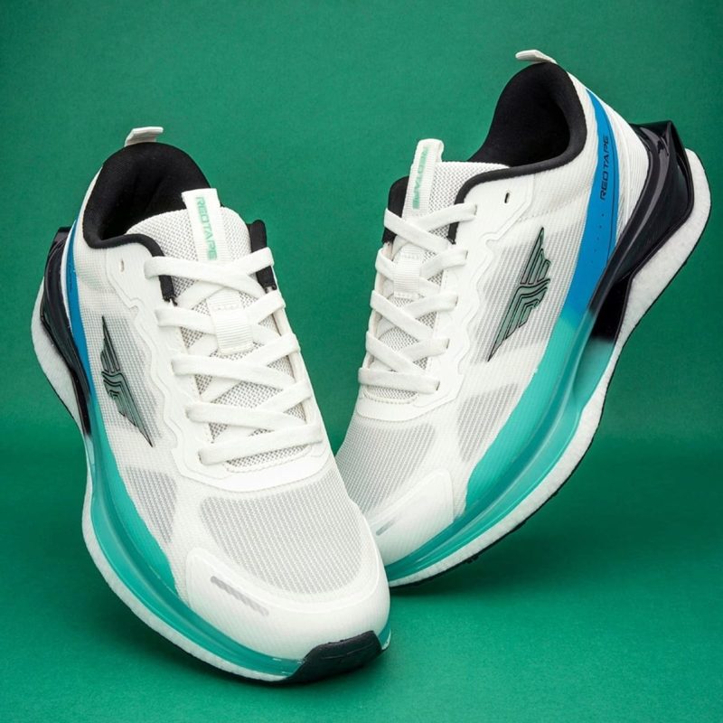 Red Tape AirFlex Pro running shoes in white and aqua blue on a green background.