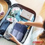 Woman packing a blue travel shoe cube containing white sneakers into her neatly organized suitcase.