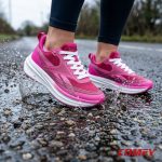 Pink and purple Reebok women's sneakers splashing water on wet pavement.